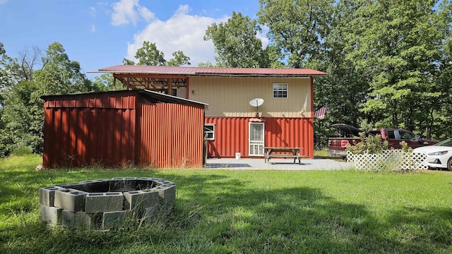 back of property with an outdoor fire pit, metal roof, a lawn, and a patio