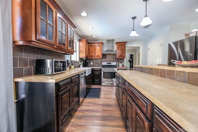 kitchen featuring decorative backsplash, wall chimney exhaust hood, appliances with stainless steel finishes, hardwood / wood-style flooring, and sink