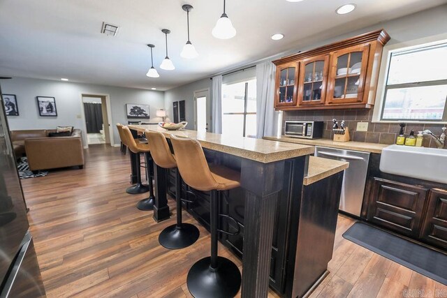 kitchen featuring tasteful backsplash, hanging light fixtures, hardwood / wood-style floors, dishwashing machine, and a center island