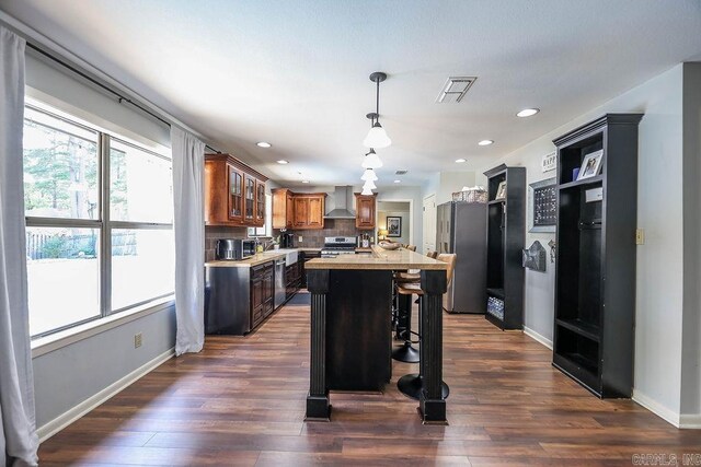 kitchen with a center island, dark hardwood / wood-style flooring, wall chimney exhaust hood, decorative backsplash, and stainless steel appliances