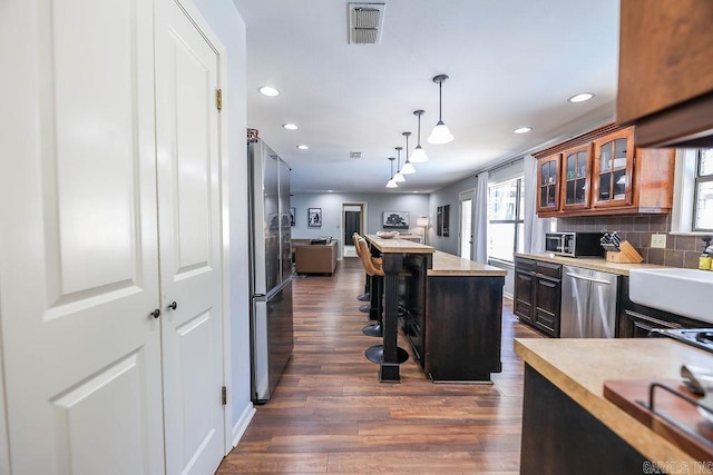 kitchen with stainless steel appliances, decorative light fixtures, decorative backsplash, dark hardwood / wood-style flooring, and a breakfast bar