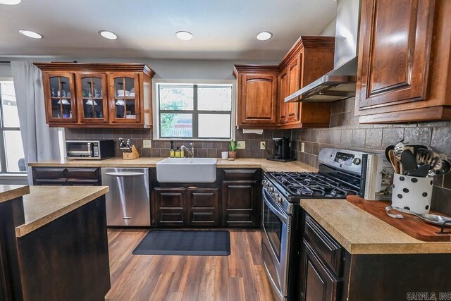 kitchen featuring hardwood / wood-style flooring, wall chimney exhaust hood, tasteful backsplash, sink, and stainless steel appliances