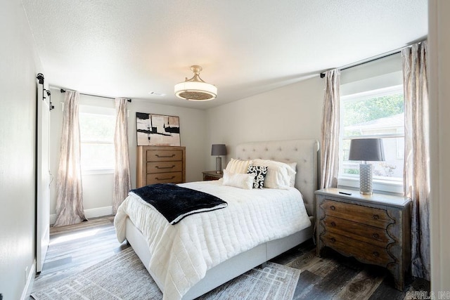 bedroom with a barn door, a textured ceiling, baseboards, and wood finished floors