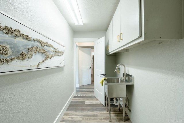 hall featuring a sink, wood finished floors, and baseboards