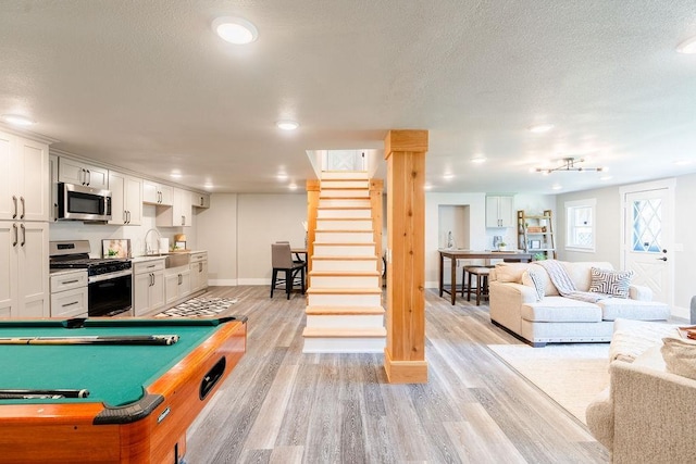 game room with light wood-style flooring, a textured ceiling, baseboards, and a sink