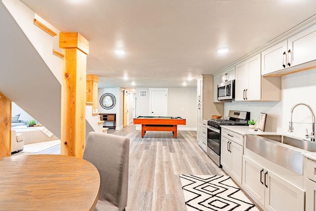 kitchen featuring light wood finished floors, stainless steel appliances, pool table, white cabinets, and a sink