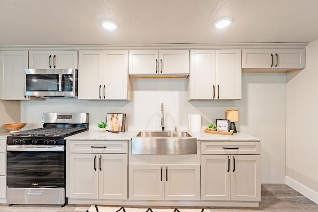 kitchen featuring light wood finished floors, white cabinetry, stainless steel appliances, and a sink