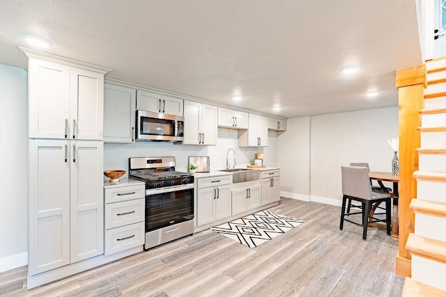 kitchen with light wood finished floors, appliances with stainless steel finishes, white cabinets, and a sink