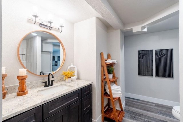 bathroom featuring toilet, baseboards, wood finished floors, and vanity