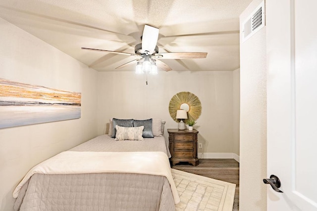 bedroom with a ceiling fan, visible vents, baseboards, and wood finished floors