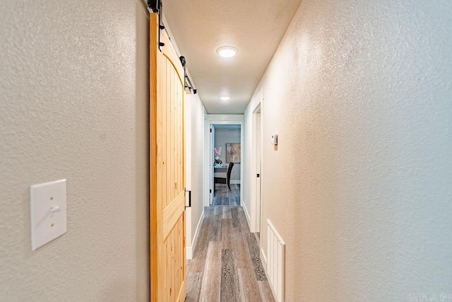 hallway featuring light wood finished floors, a textured wall, a barn door, and visible vents