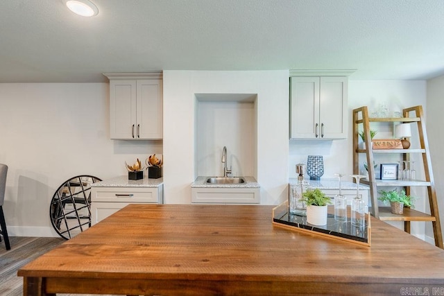 kitchen with baseboards, white cabinets, light stone counters, wood finished floors, and a sink