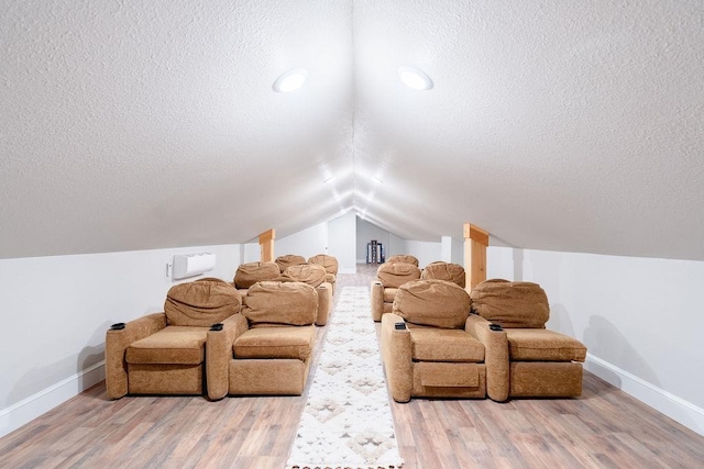 cinema room with a textured ceiling, baseboards, vaulted ceiling, and wood finished floors