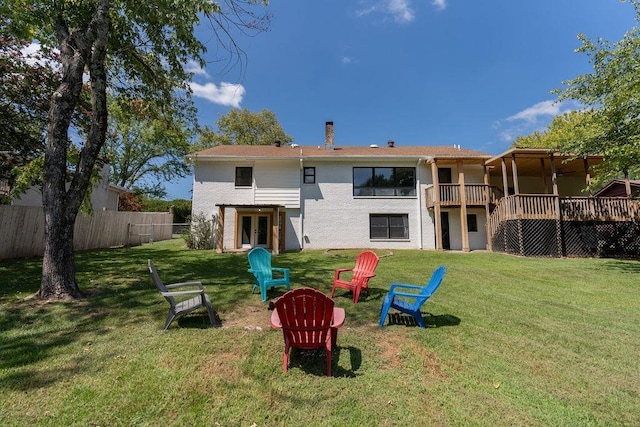 back of house with a chimney, a lawn, an outdoor fire pit, fence, and a wooden deck