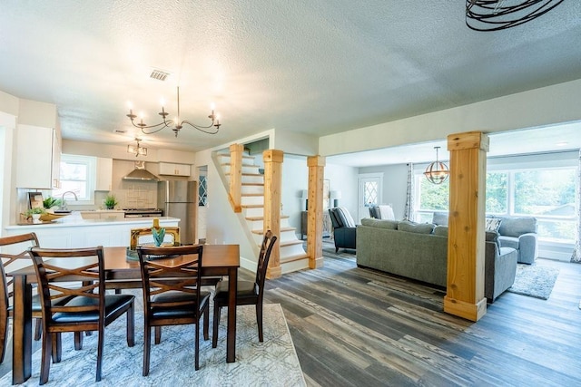 dining area with visible vents, stairway, an inviting chandelier, dark wood-type flooring, and ornate columns