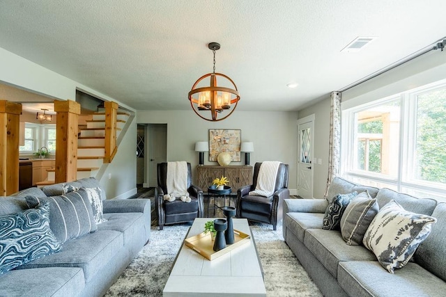 living room featuring visible vents, stairway, a chandelier, and a textured ceiling