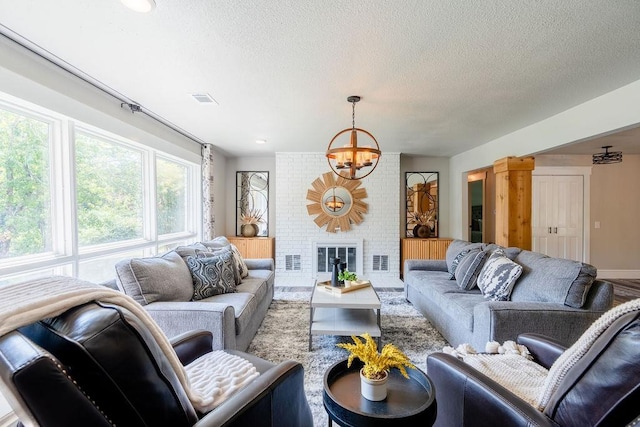 living room with an inviting chandelier, a brick fireplace, visible vents, and a textured ceiling