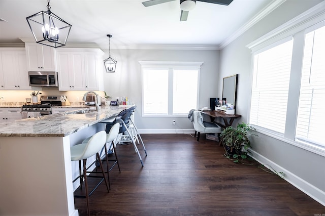 kitchen with kitchen peninsula, hanging light fixtures, ornamental molding, appliances with stainless steel finishes, and white cabinets