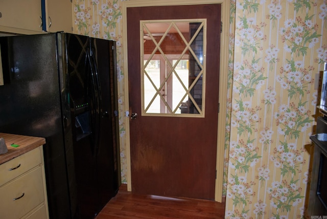 kitchen with black refrigerator with ice dispenser, wallpapered walls, and wood finished floors