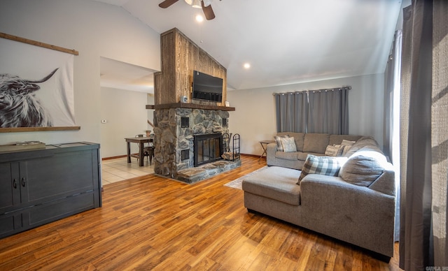 living room with ceiling fan, light hardwood / wood-style floors, a stone fireplace, and lofted ceiling