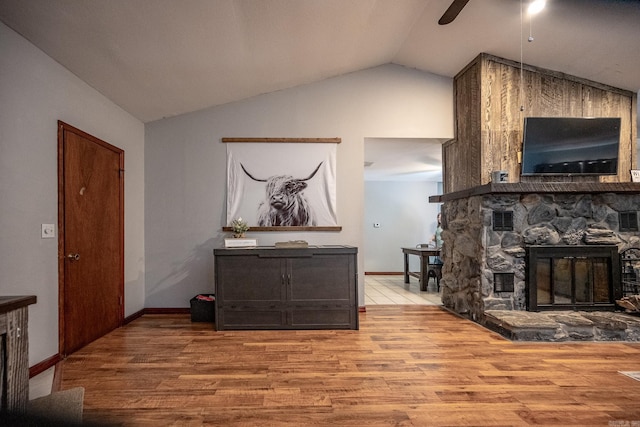 living room featuring light wood-type flooring, a stone fireplace, ceiling fan, and lofted ceiling