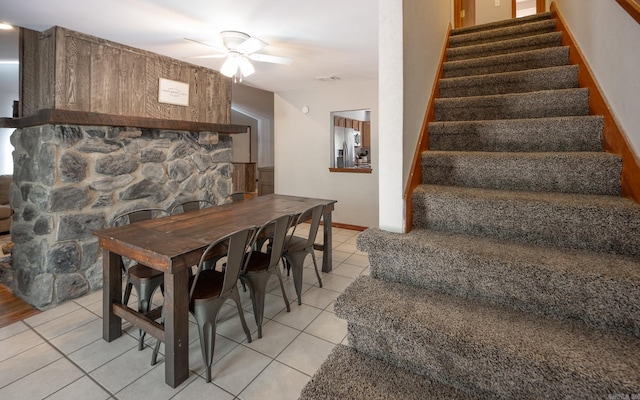 tiled dining space featuring ceiling fan and a fireplace