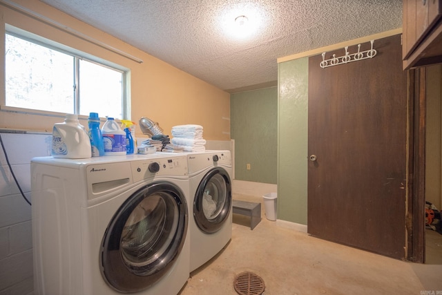 clothes washing area with washer and dryer, a textured ceiling, and cabinets