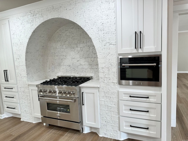 kitchen featuring appliances with stainless steel finishes, white cabinetry, light hardwood / wood-style flooring, and light stone counters