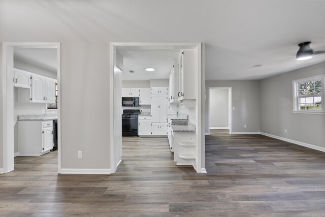 kitchen featuring hardwood / wood-style floors, light stone countertops, white cabinetry, and black appliances