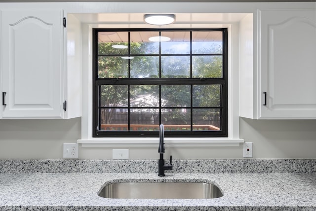 details with white cabinetry, a sink, and light stone countertops