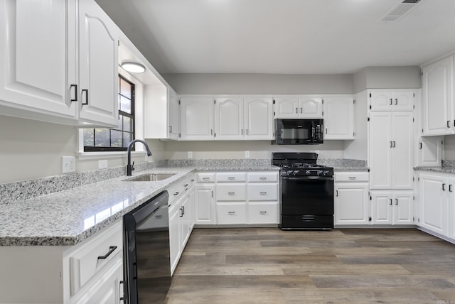 kitchen featuring black appliances, light stone counters, white cabinets, and a sink