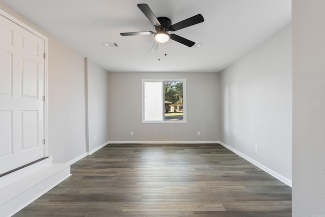 empty room featuring dark wood-type flooring, a ceiling fan, visible vents, and baseboards