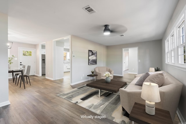 living area featuring visible vents, ceiling fan, baseboards, and wood finished floors