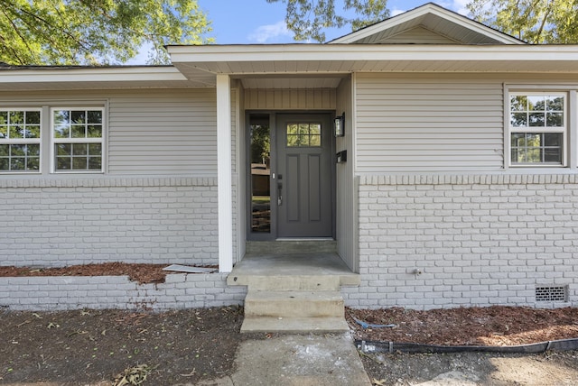 view of exterior entry featuring brick siding and crawl space