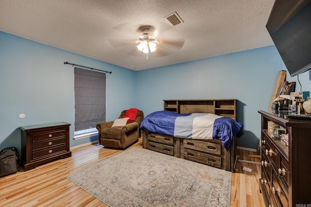 bedroom with visible vents, a barn door, a ceiling fan, a textured ceiling, and light wood-type flooring