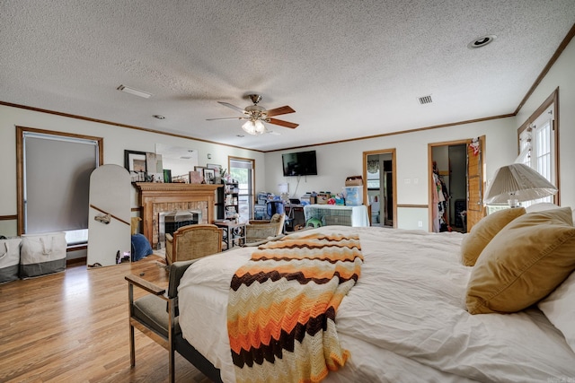 bedroom featuring a textured ceiling, ornamental molding, a fireplace, and light wood-style floors