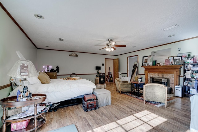 bedroom with crown molding, a fireplace, visible vents, and wood finished floors