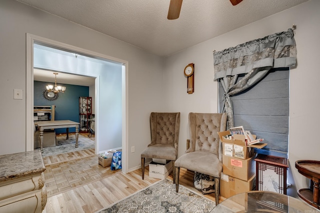 living area featuring a textured ceiling, baseboards, wood finished floors, and ceiling fan with notable chandelier