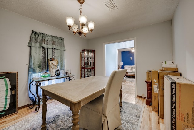 dining area with a chandelier, a textured ceiling, visible vents, baseboards, and light wood-style floors