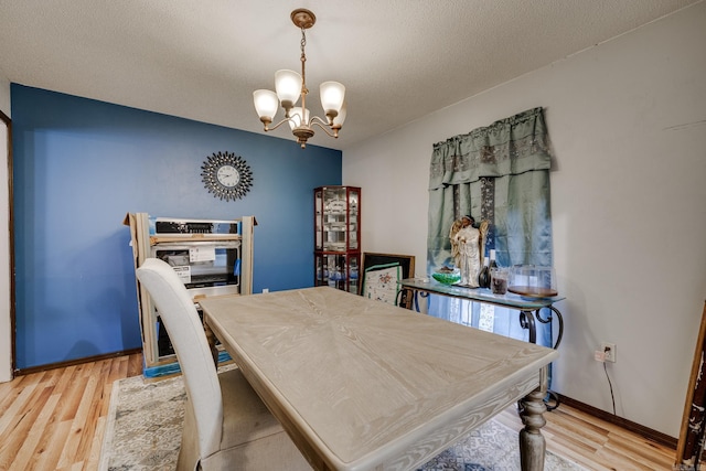 dining area with a chandelier, baseboards, light wood-style flooring, and a textured ceiling