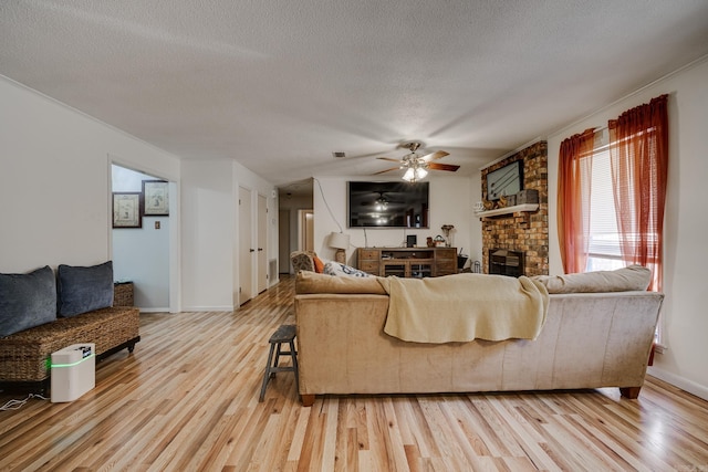 living area featuring a textured ceiling, a fireplace, visible vents, a ceiling fan, and light wood finished floors