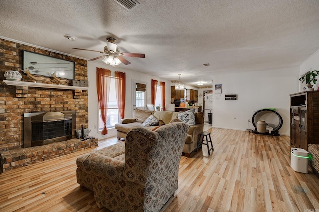 living room featuring ceiling fan, a textured ceiling, light wood-style flooring, visible vents, and a brick fireplace