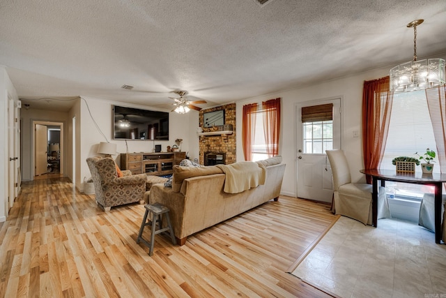 living area featuring a textured ceiling, light wood-type flooring, ceiling fan with notable chandelier, and a fireplace