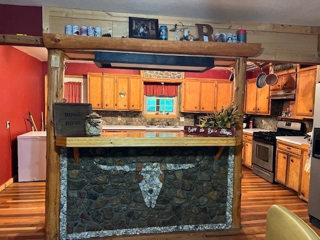 kitchen with hardwood / wood-style flooring, washer / dryer, stainless steel gas range, and tasteful backsplash