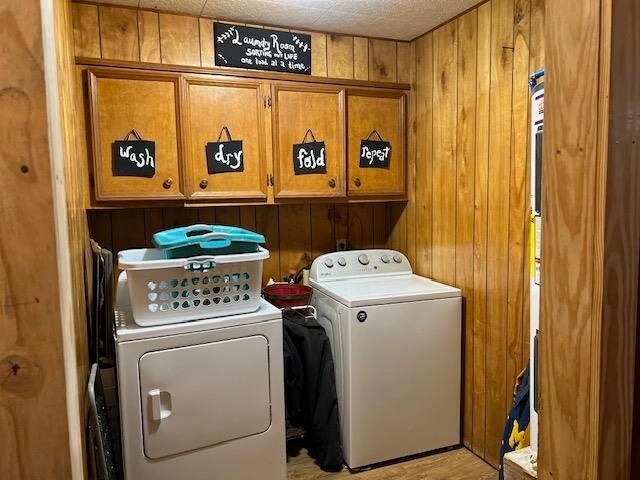 clothes washing area featuring wood walls, washer and clothes dryer, and cabinets