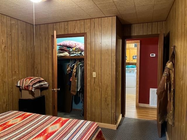 bedroom with a closet, wood walls, washer / clothes dryer, and hardwood / wood-style floors