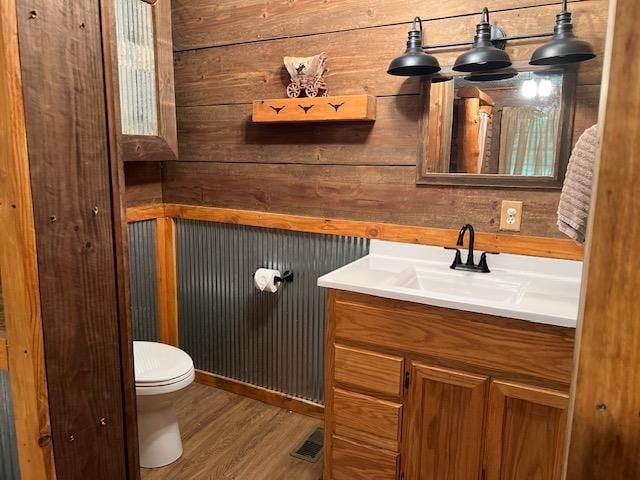 bathroom featuring wood walls, hardwood / wood-style floors, toilet, and vanity