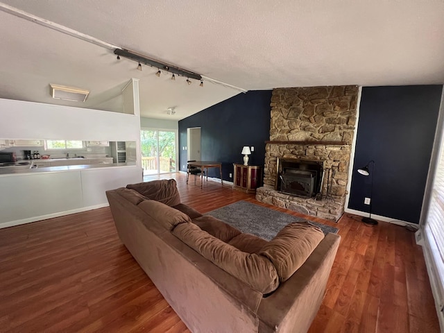 living room featuring a stone fireplace, hardwood / wood-style floors, rail lighting, a textured ceiling, and lofted ceiling