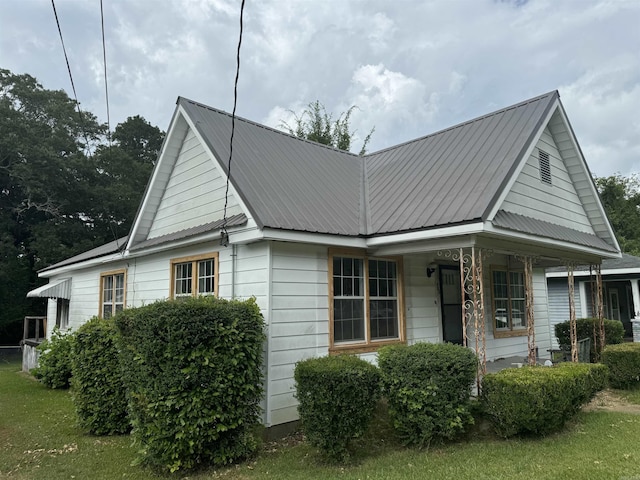 view of front of home featuring covered porch, a front lawn, and metal roof