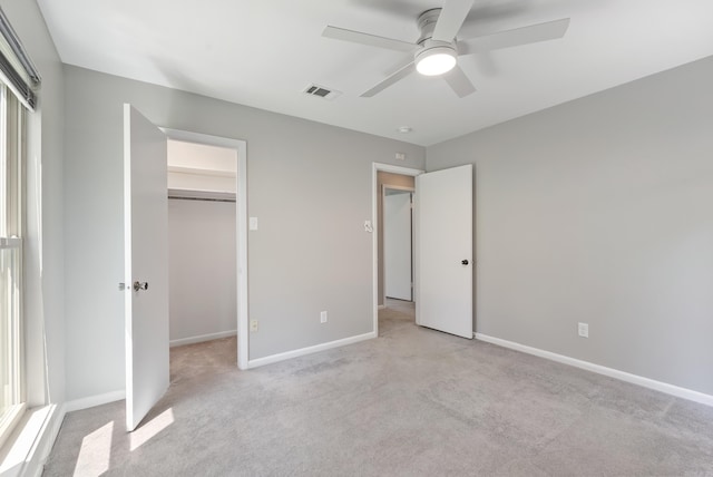 unfurnished bedroom with ceiling fan, a closet, light colored carpet, and a walk in closet